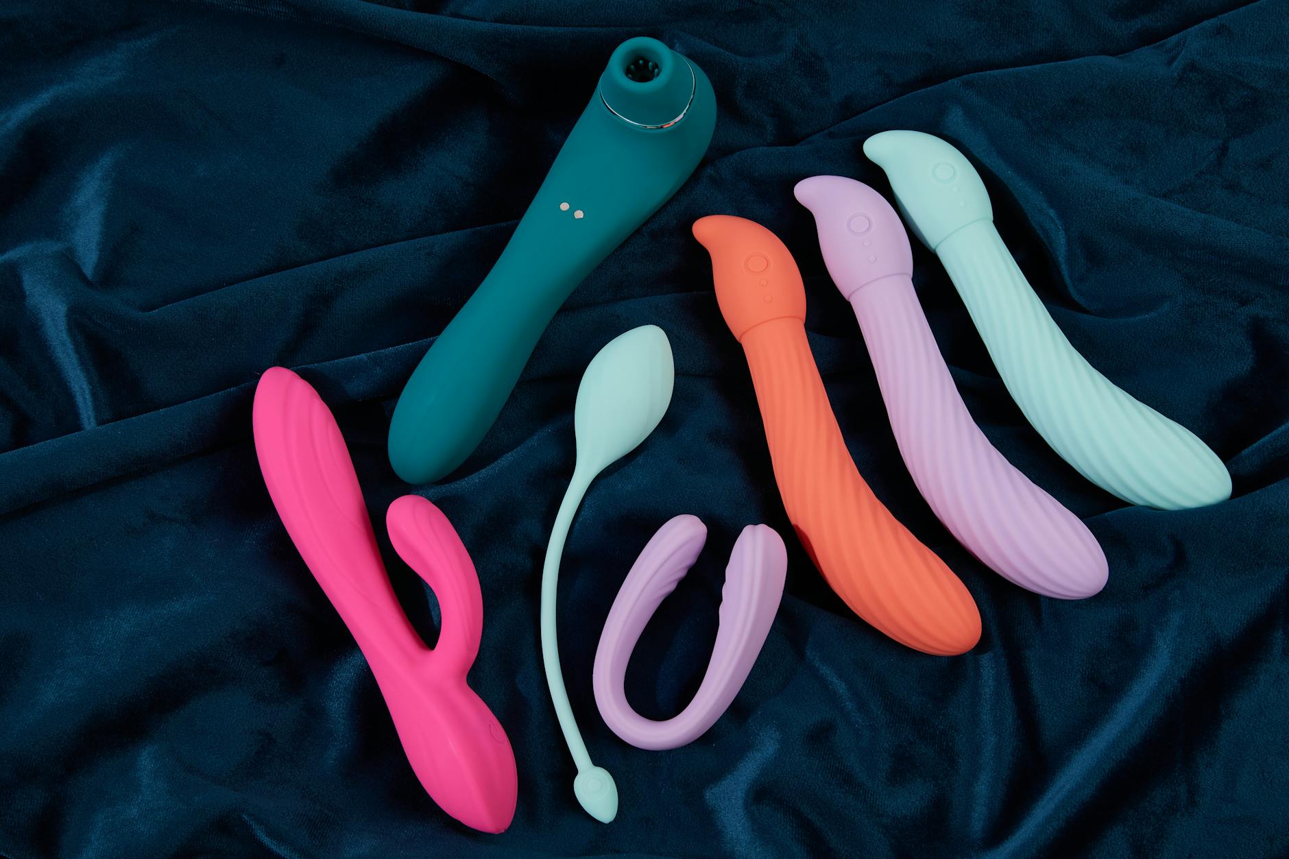 Hand holding a blue silicone clitoral vibrator against a purple background