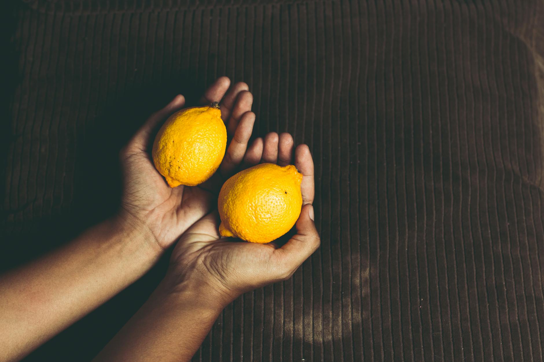 Two fresh lemons held gently in cupped hands, symbolizing tenderness and self-care