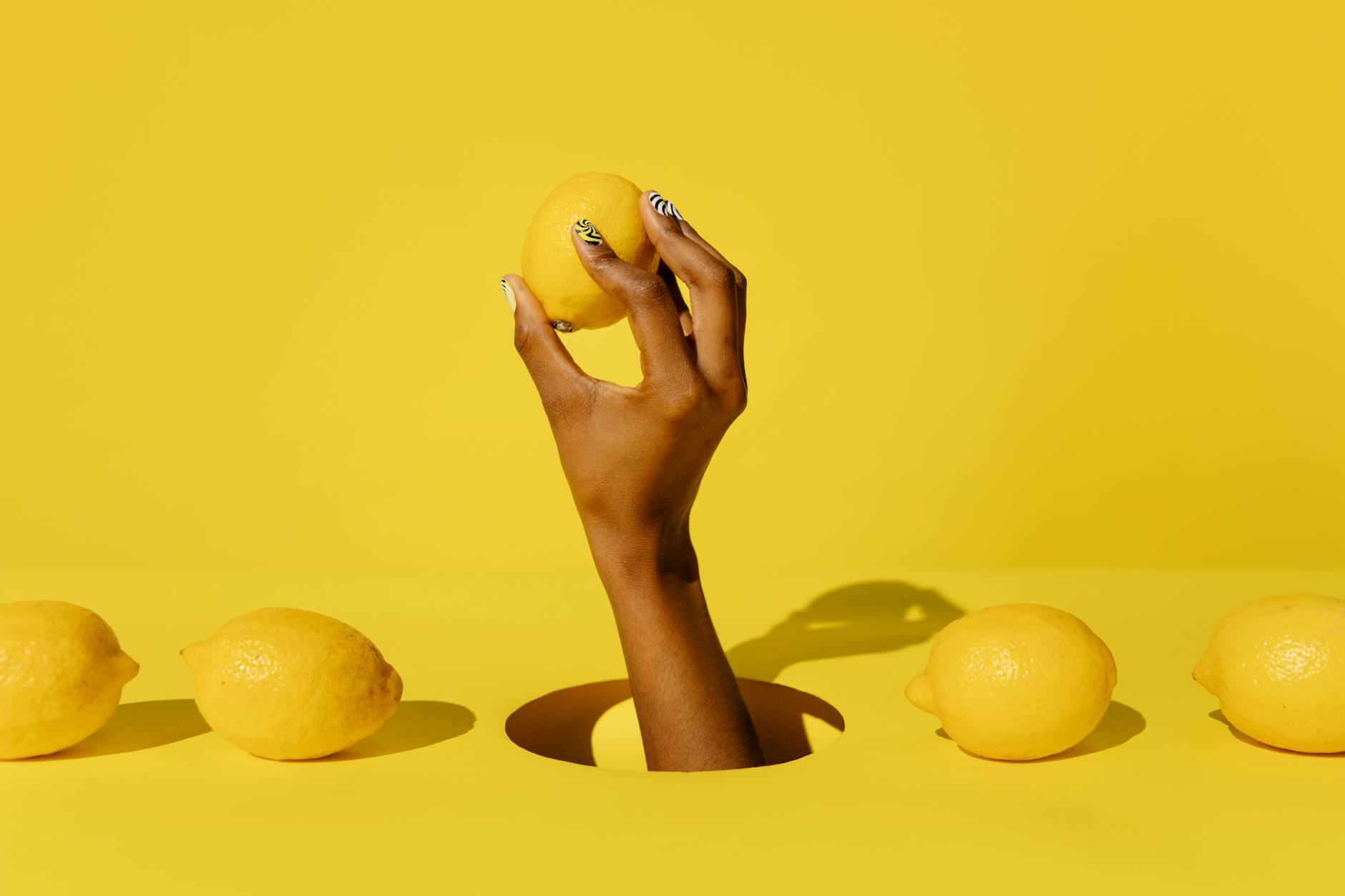 A hand holding a fresh lemon against a bright yellow background, representing clarity and fresh perspectives on introducing toys to partners