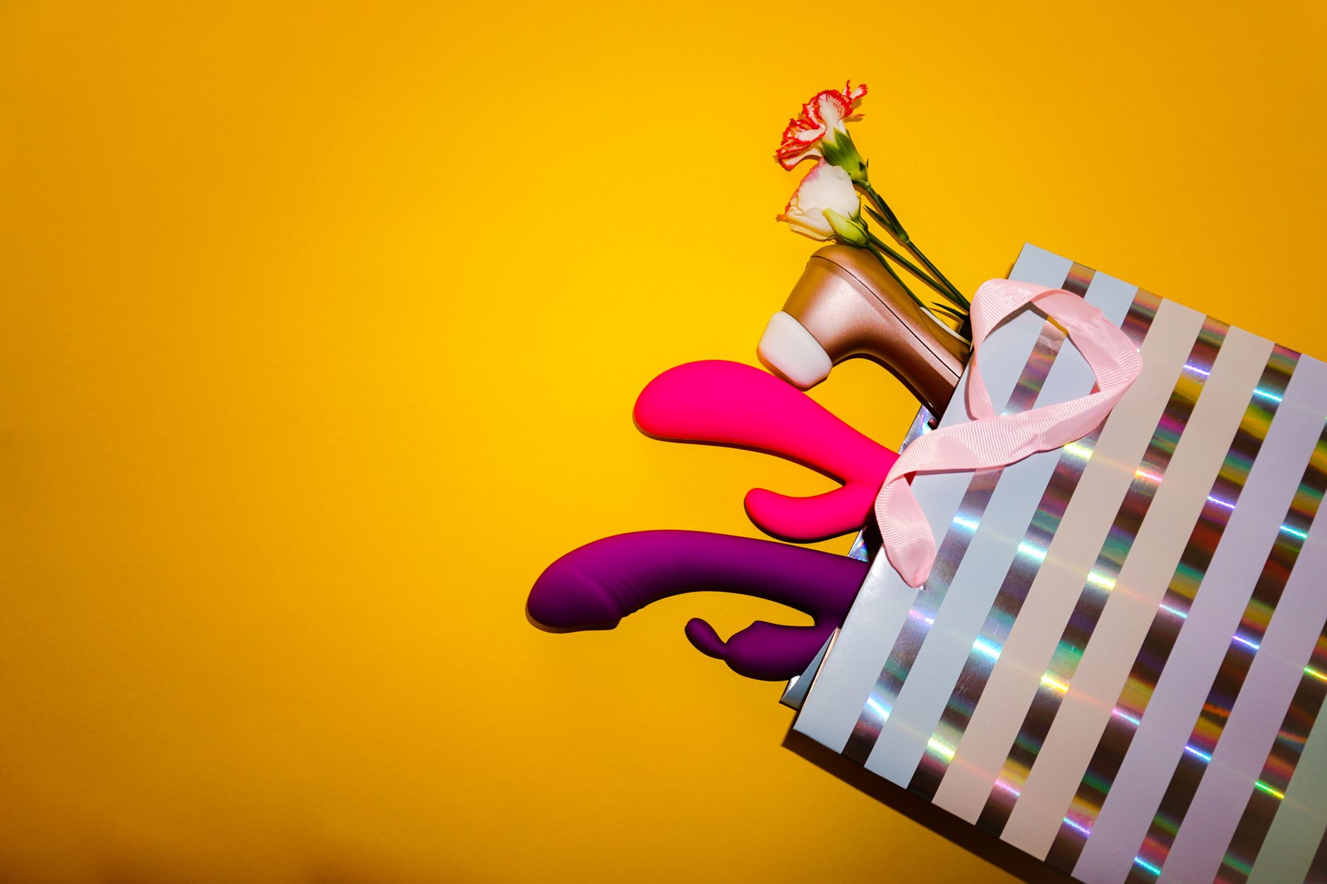 Colorful clitoral vibrators displayed with flowers on a bright yellow background